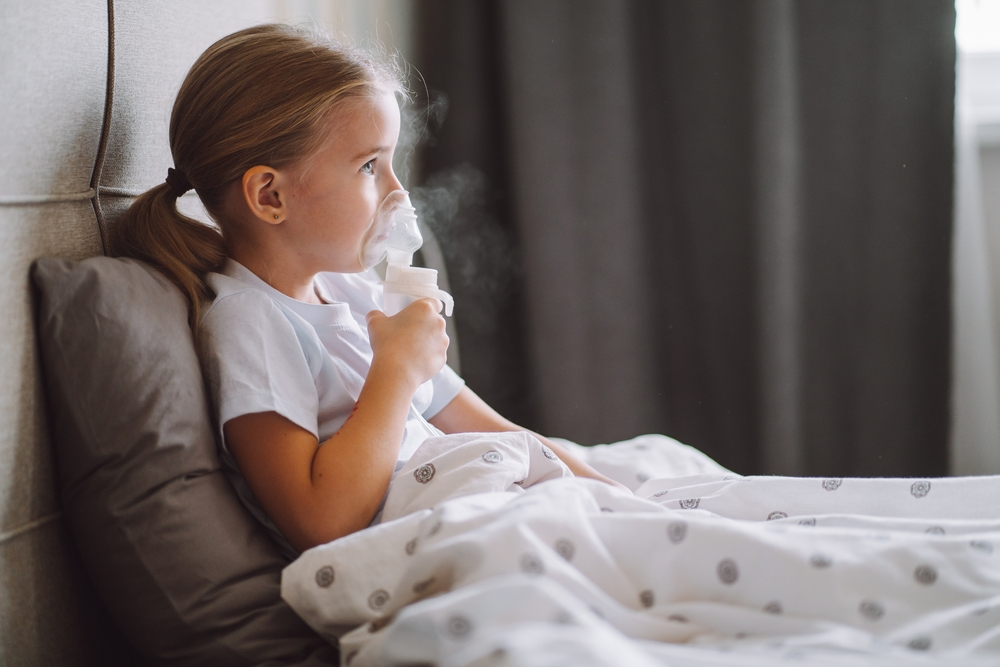 Little girl use inhaler nebulizer lying in bed. shutterstock_2094377605